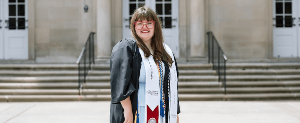 Gracy Kelly, 2024 commencement speaker, stands in her robe and cords outside of Keen Johnson on campus.