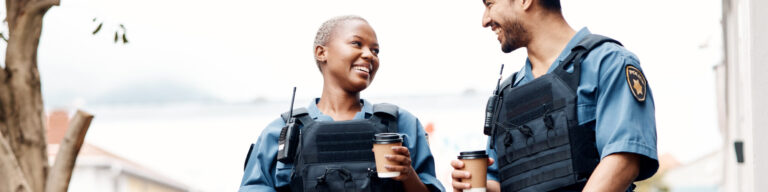 police officers wearing bullet proof vests talk outside as they hold cups of coffee