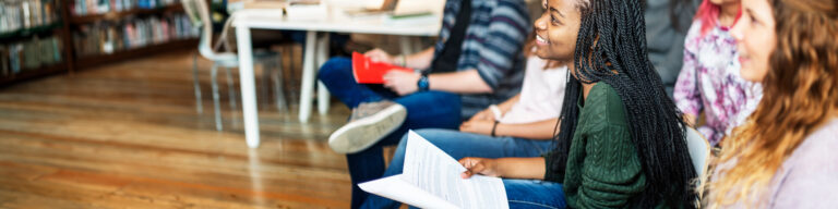 a smiling group of students sit and listen to someone in a philosophy class as one student holds an open book