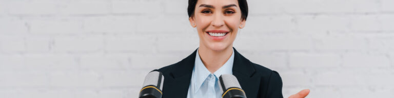 a professionally dressed woman stands at two microphones set up for her to speak