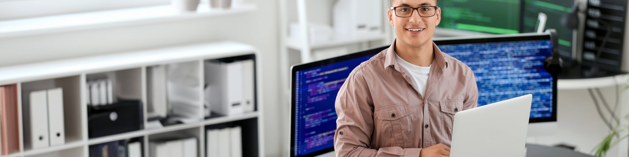 a student uses a laptop while computer programming displays on monitors behind him