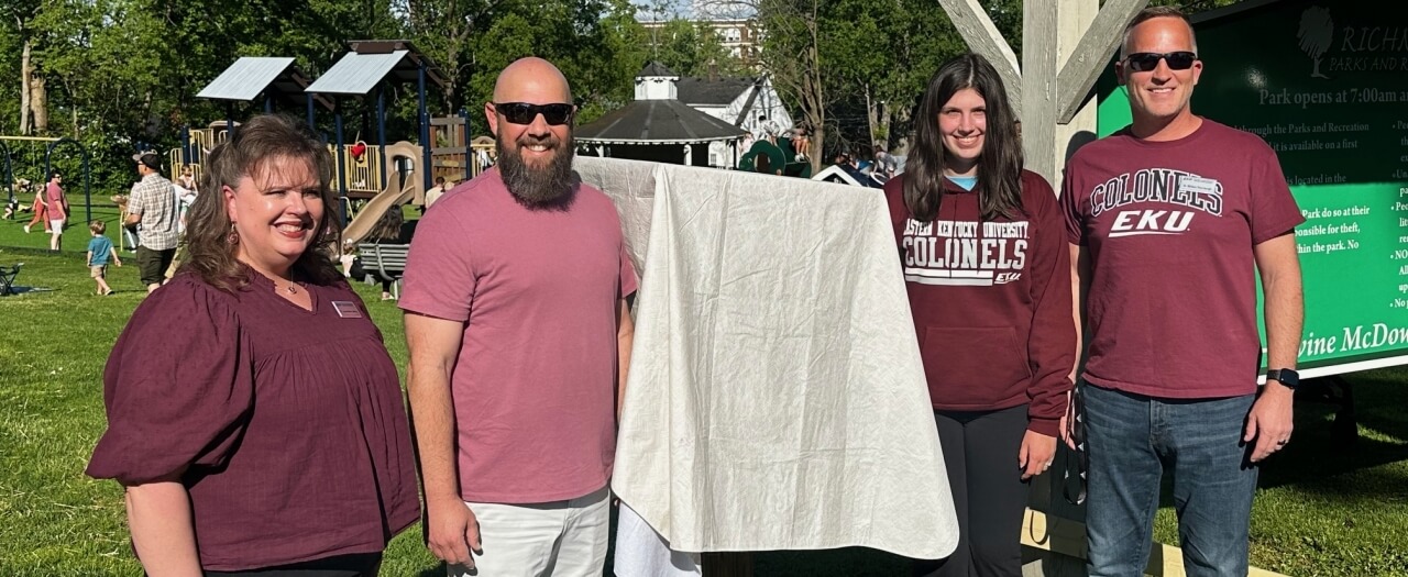 Contributors stand next to the covered box, waiting to unveil the Little Free Library at a local park.