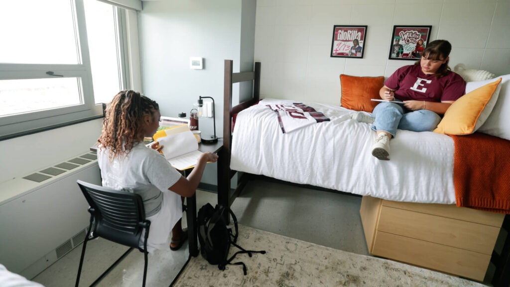 in a shared room in Keene Hall one student sits at a study table while another student sits on a lofted bed