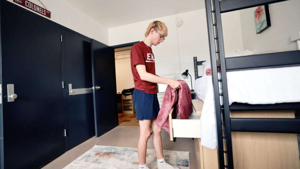 a student puts a blanket in a drawer below a lofted bed across from a closet in a shared room in Mattox Hall