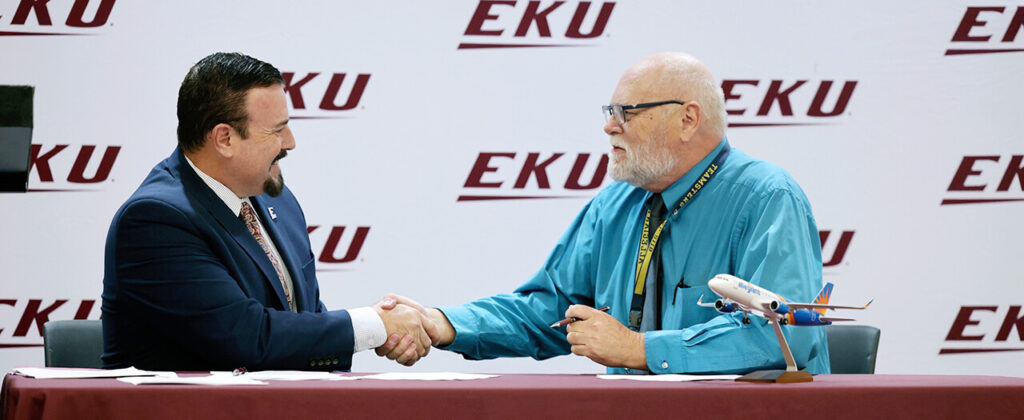 EKU president David McFaddin shakes hands with Allegiant Air's Tyler Hollingsworth, senior vice president of Flight Operations at a press conference in front of an EKU backdrop