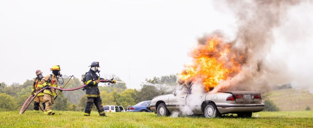 A team of fire students use a hose to extinguish a burning car at EKU's outside fire lab training center