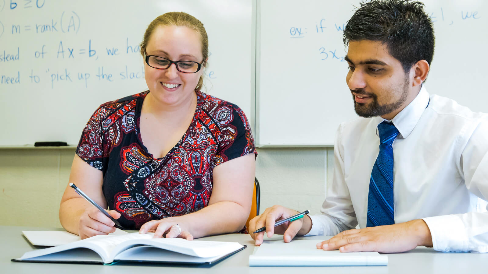 two students making notes in front of whiteboards with math formulas written on them