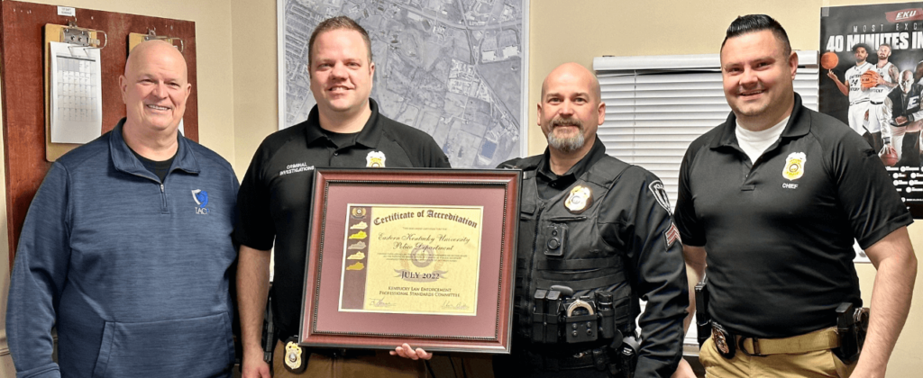 Three EKU police officers pose with a member of the Kentucky Association of Chiefs of Police and a framed certificate of appreciation.