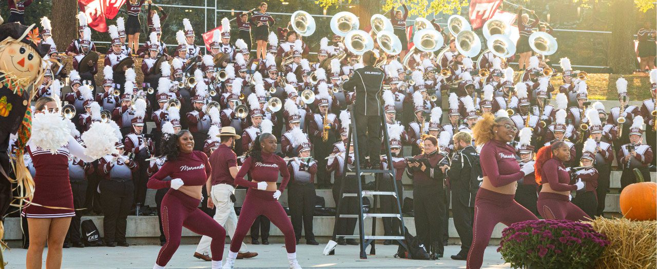 the marching band performs on risers as the Maroonettes dance