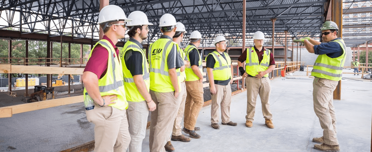 EKU professor addresses EKU students in yellow safety vests and hard hats on a construction site.