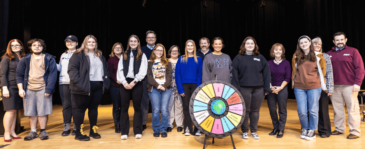 A large group of EKU students stand on stage with faculty and administration with spinning wheel for the Spin the Wheel Scholarship awards.