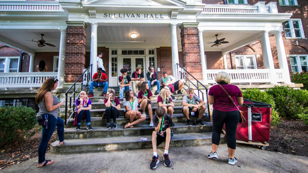 students sitting on the front steps of Sullivan Hall with columns and porch fans in view