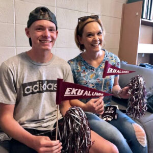 EKU grad and mom Angela Short and her son, an EKU student, in his dorm room holding EU pennants and pom poms.