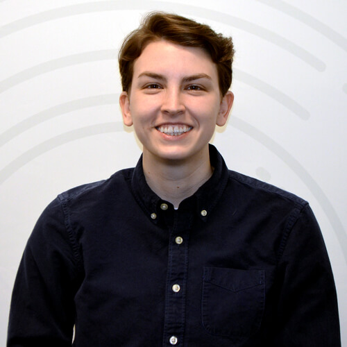 EKU business student Jessica Wagner, in a navy button down shirt, stands in front of a white geometric background for a photo.