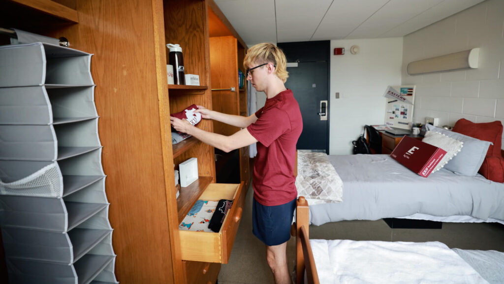 a student puts clothes in a cabinet beside a closet in a shared room in Clay Hall