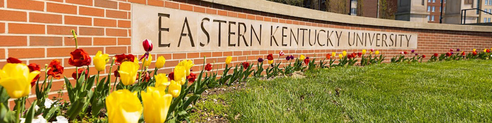 a brick sign that says Eastern Kentucky University with yellow and red tulips blooming in front of it