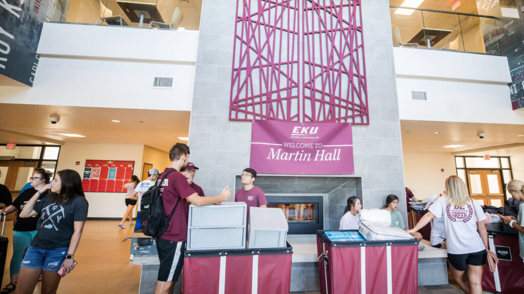 students and families rolling carts into the lobby of Martin Hall on move-in day a fireplace and bulletin board and upper floor sitting area are shown