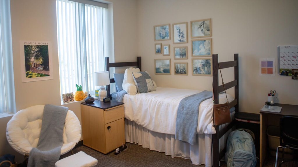 one half of a shared bedroom in Martin Hall with a bed and chair and cabinet and a desk and windows