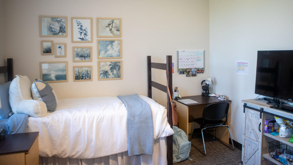 one half of a shared bedroom in Martin Hall with a bed and cabinet and desk and a TV on a cabinet