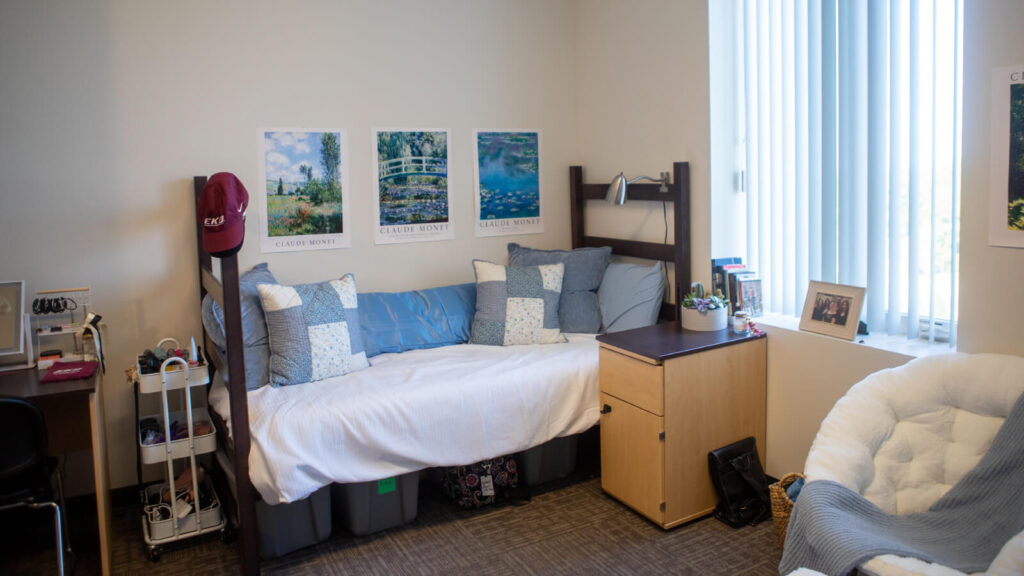 one half of a shared bedroom in Martin Hall with a bed and under bed storage and a desk and cabinet and windows and a chair