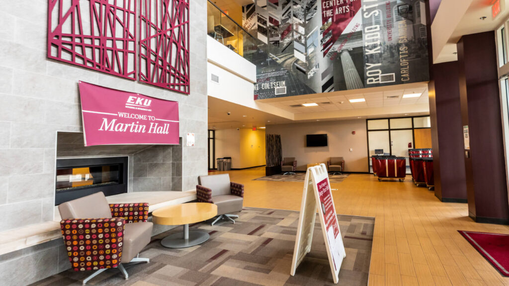 inside the entrance of Martin Hall with tables and chairs and a TV and a fireplace and a view of more tables and chairs on the next floor