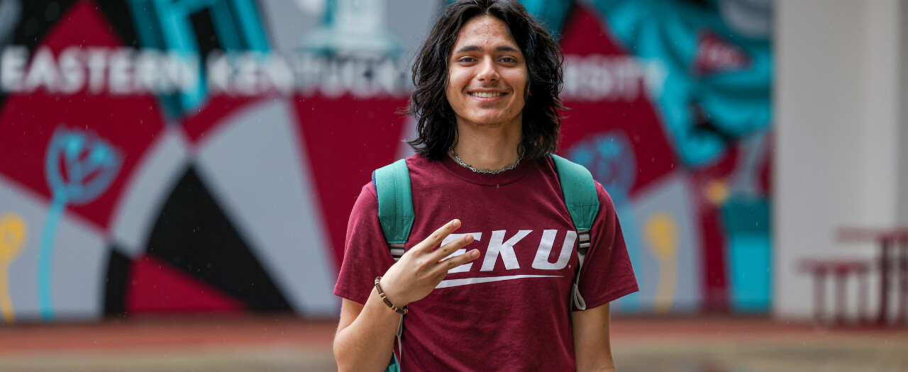 EKU Transfer student Alexander Zacarias flashes the Big E hand sign in front of the colorful mural at Powell Student Plaza.