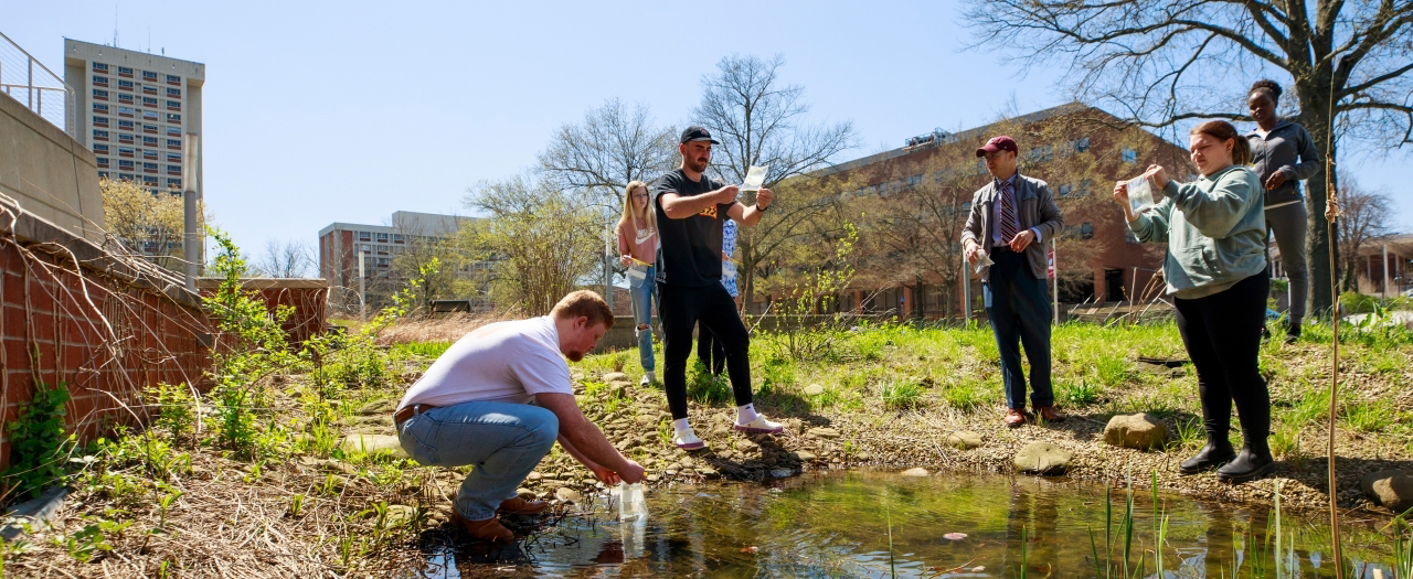 A group of male and female students collect water samples on EKU's campus with their professor.