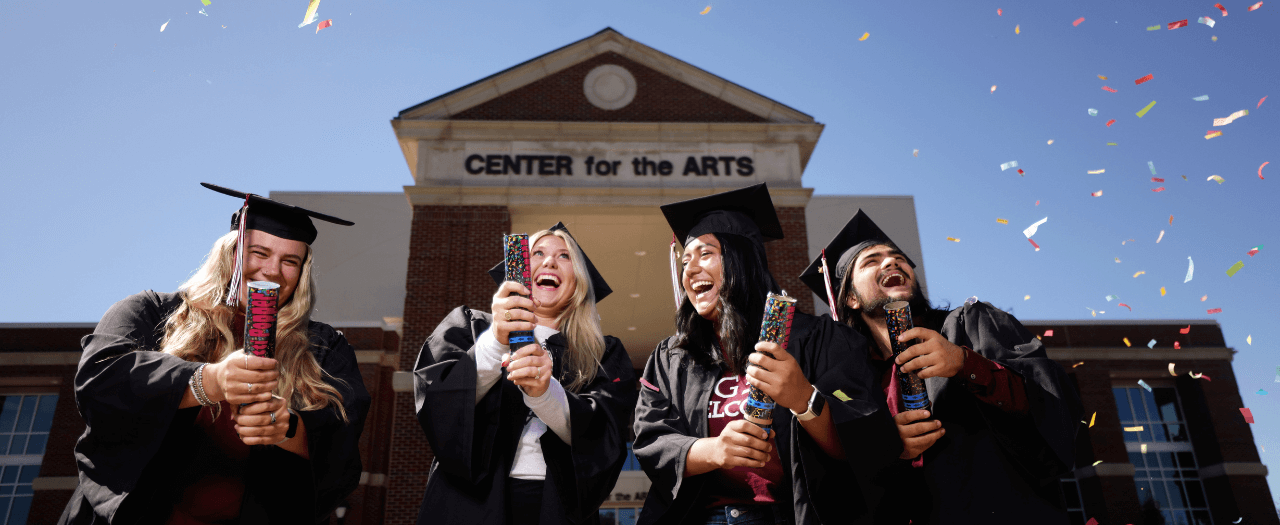 EKU students in caps and gowns in front of EKU's Center for the Arts celebrate with smiles and confetti.