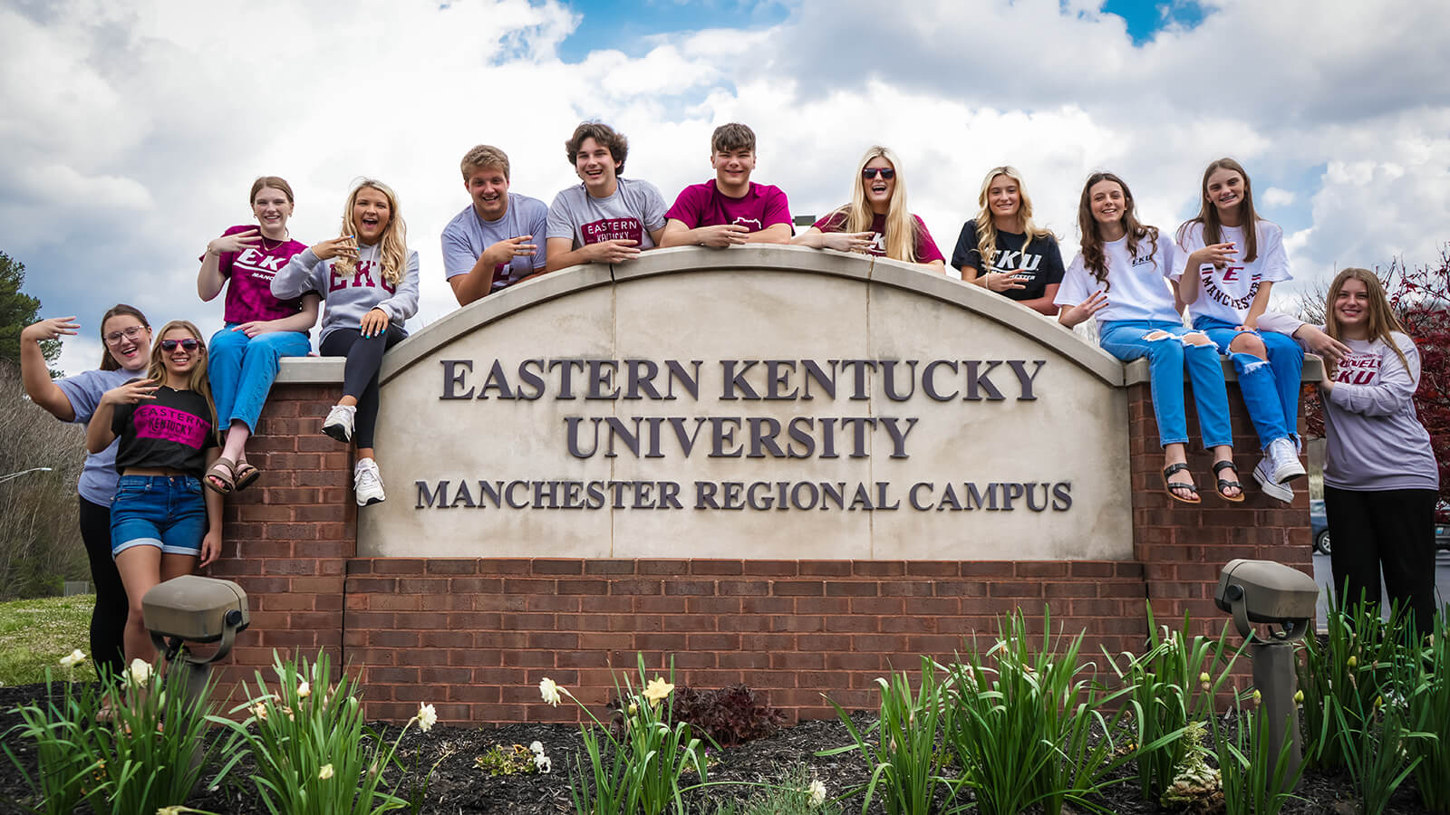 A group of smiling EKU students, wearing a variety of EKU t-shirts gather around the Manchester Regional Campus entrance.