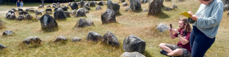 two students in a field with boulders, taking notes and photos