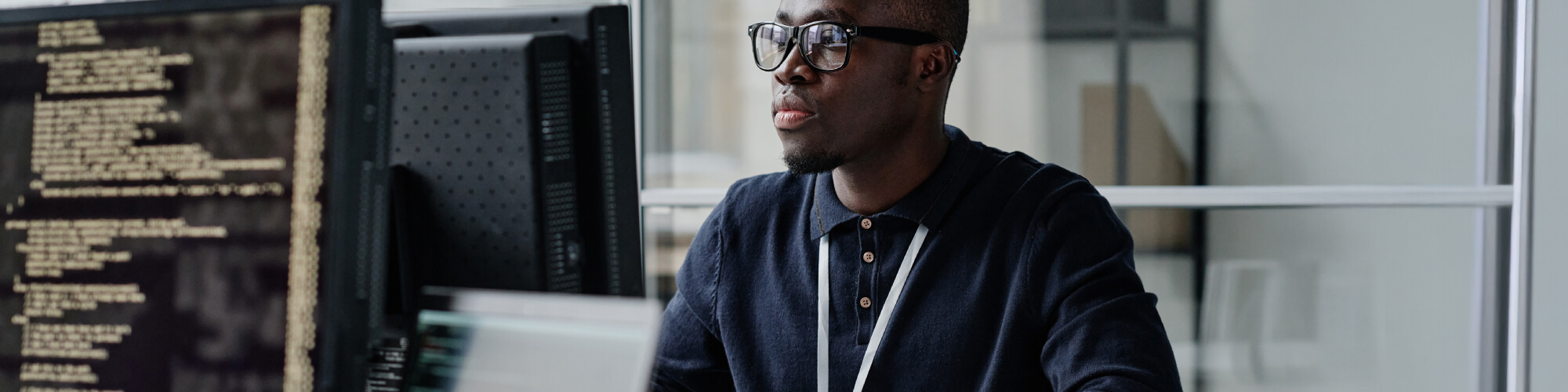 close up of a student sitting in a computer lab looking at computer screen. A different computer screen facing the camera displays programming code