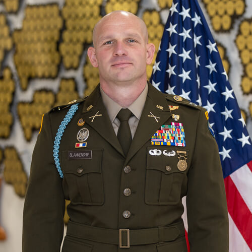 Photo of Captain Corey Blankenship in official dress uniform standing in front of the US flag.