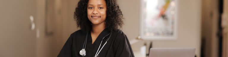 EKU nursing student with stethoscope smiles at the camera while standing in the hallway of a hospital