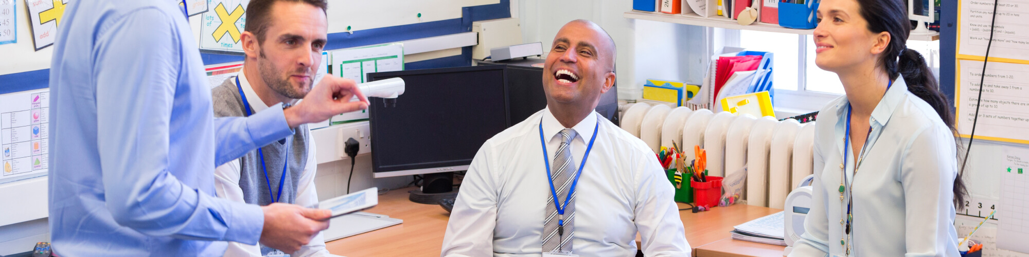 group of teacher administrators in lanyards talking and laughing while in a school office