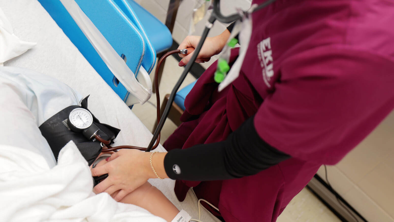 close up of an EKU nursing student checking the blood pressure of a patient manikin in a bed with blood pressure cuff and stethoscope